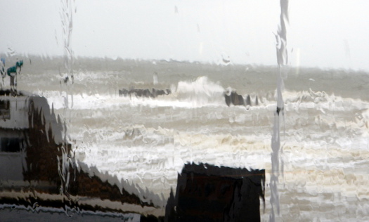 rough sea behind water-soaked window