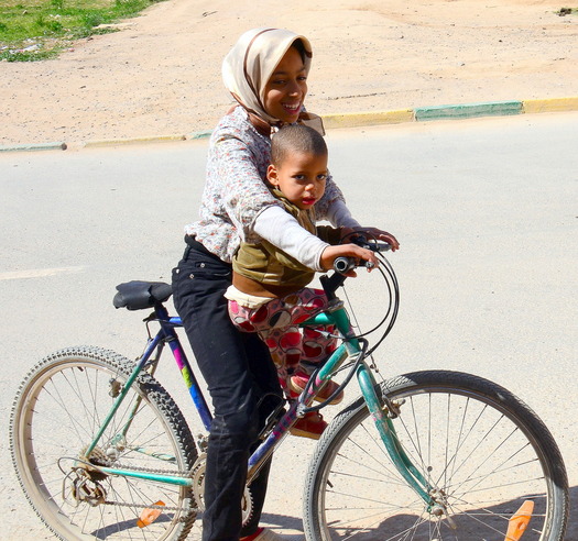 smiling woman on a bicycle with small child sitting on the crossbar