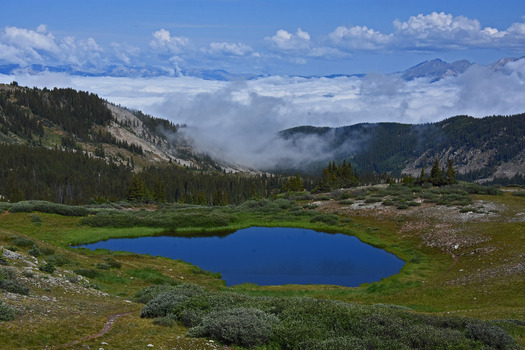 Apline scene with a lake that has small cloud hanging over it