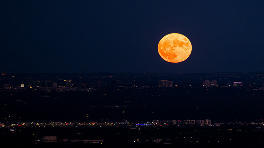Orange full Moon over human lights at night