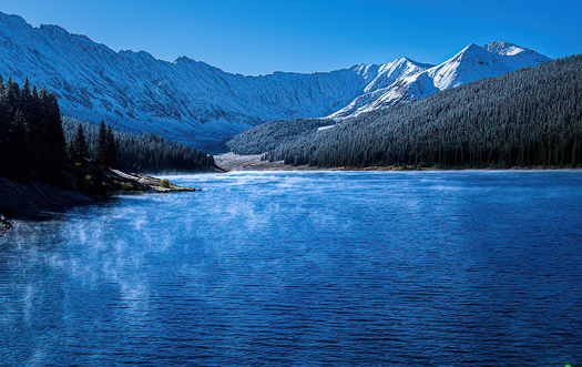 Steam rising from a lake in front of snow-covered mountains