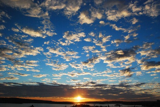 Sun at the horizon with many small clouds above.