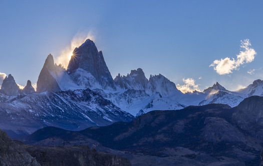 Sharp peak of snowy mountain with sun behind it
